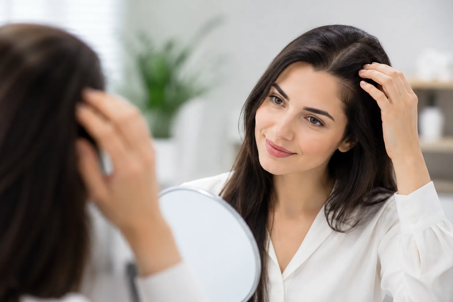A woman checking her hairline in a mirror at a hair-restoration clinic